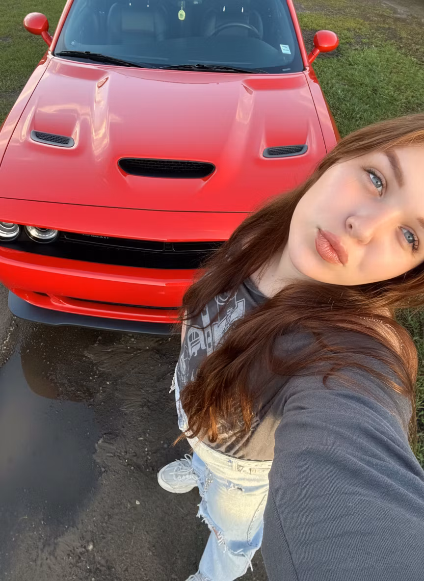 Lana Angert – Replace the dark-colored Honda SUV parked beside the young woman with a vibrant red Dodge Challenger muscle car in th…