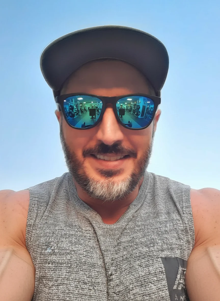 Mossi Bratini – Transform this person into a professional bodybuilder while maintaining their facial features, beard, cap, and sungla…