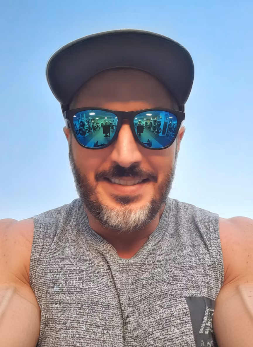 Mossi Bratini – Transform this person into a professional bodybuilder while maintaining their facial features, beard, cap, and sungla…
