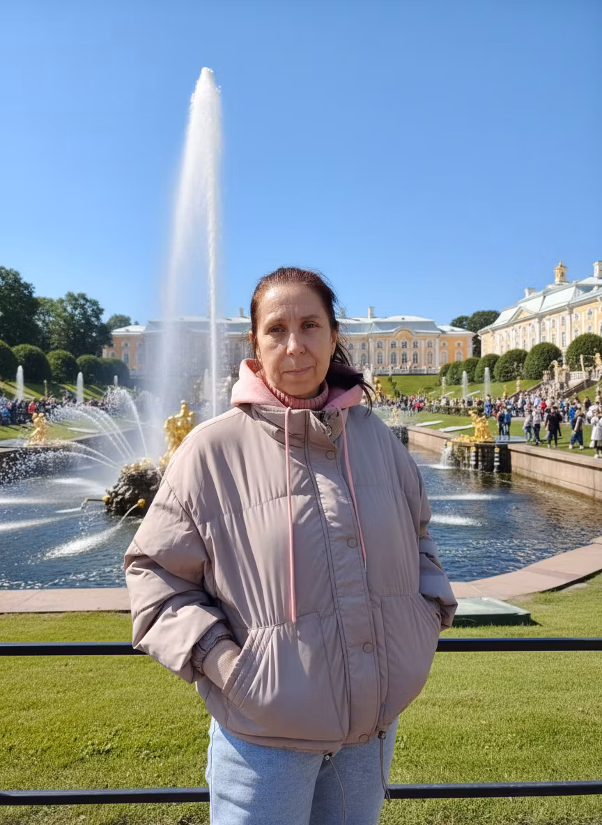Лариса Примоченко – A casual woman with light skin, dark hair tied back, wearing a beige/pale pink padded jacket with pink drawstrings, p…
