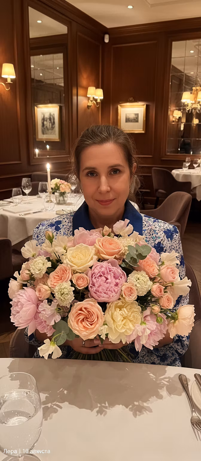 Лариса Примоченко – A beautiful young woman in an elegant restaurant setting, holding a large, luxurious bouquet of mixed flowers - roses…