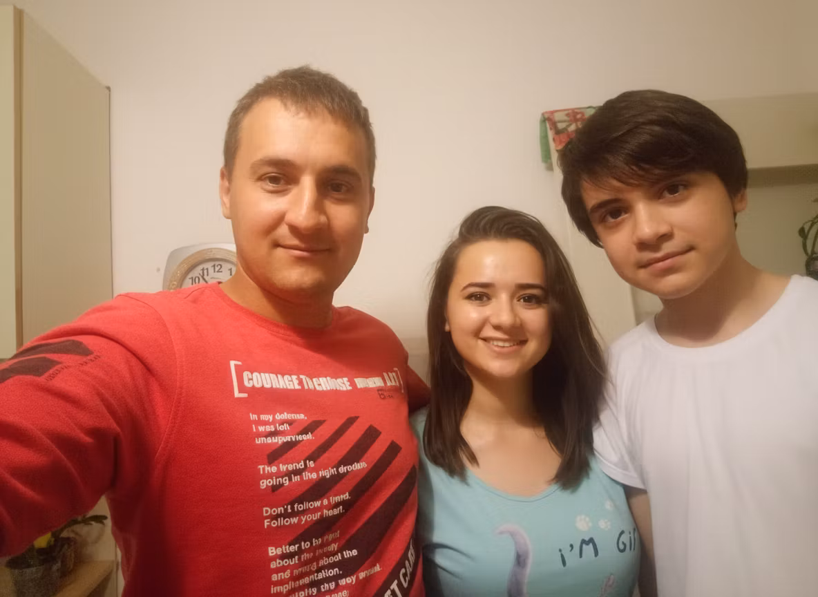 Марина Аманова – A heartwarming family portrait in a cozy indoor setting, featuring a smiling adult man with short light-brown hair in…