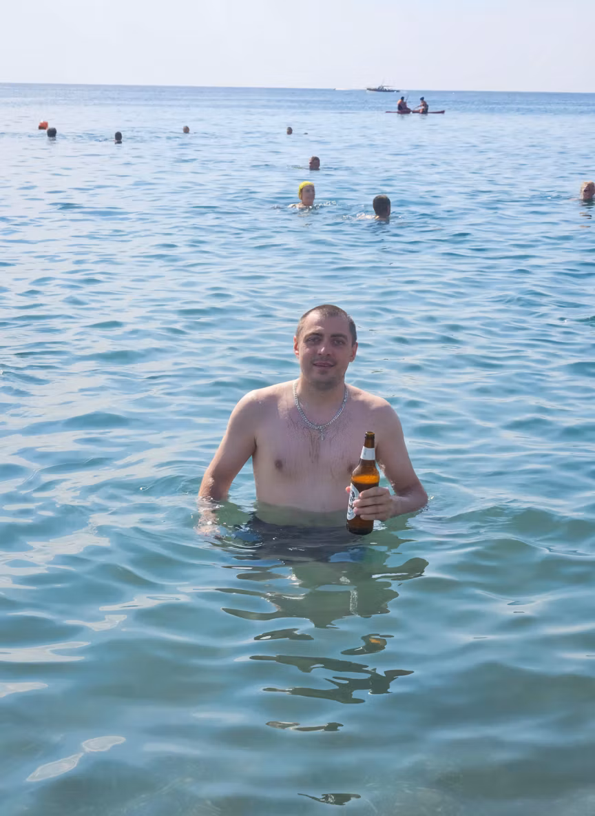 Михаил Сысоев – Using the provided image of the man standing in shallow seawater, add a cold beer bottle in his right hand. The man s…